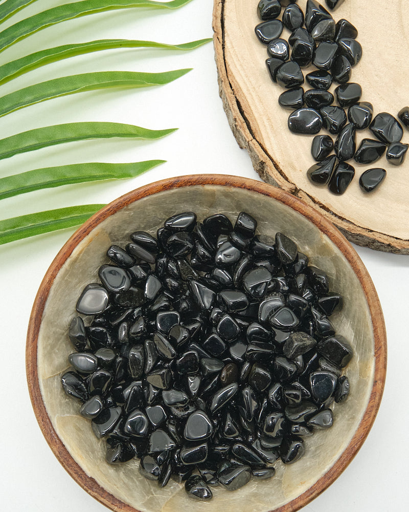 Black Obsidian stones in a ceramic bowl with a wooden slice and green leaves on a white background