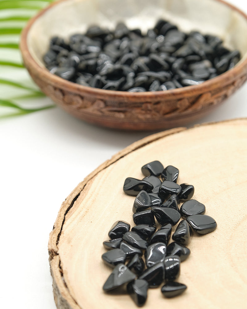 Black Obsidian stones on a wooden surface with a bowl of stones in the background